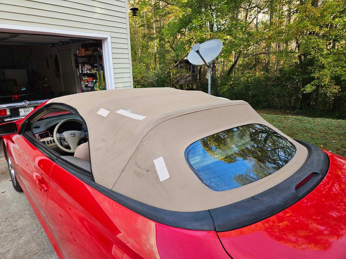 Red convertible car with tan top parked in front of a garage.