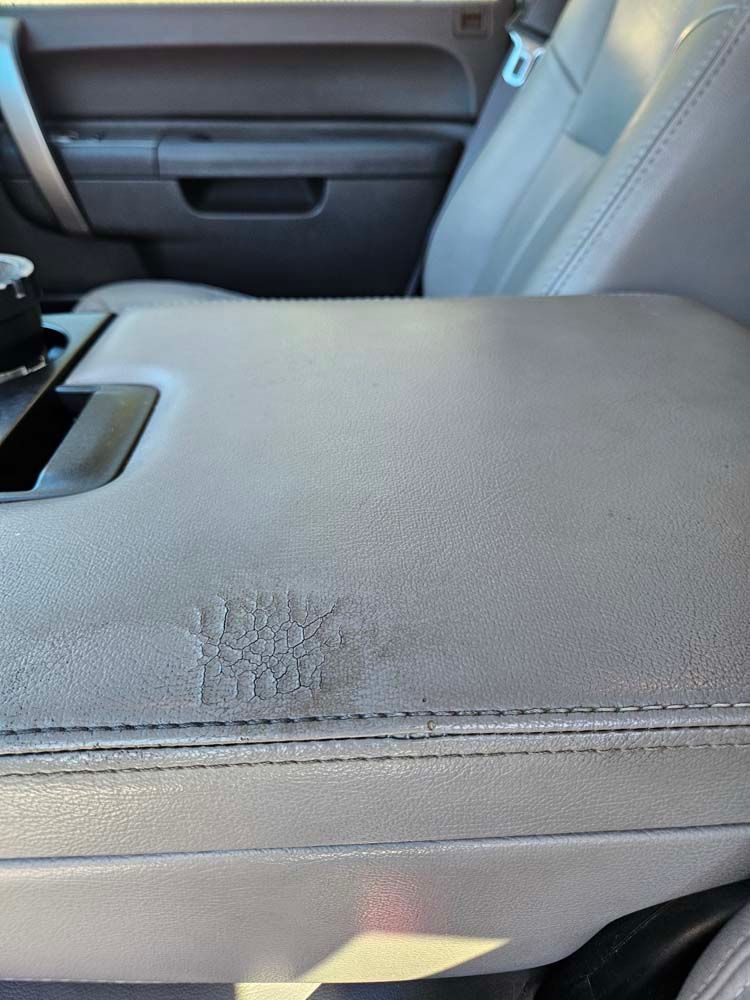 Gray car interior with worn center console armrest. Visible stitching and text.