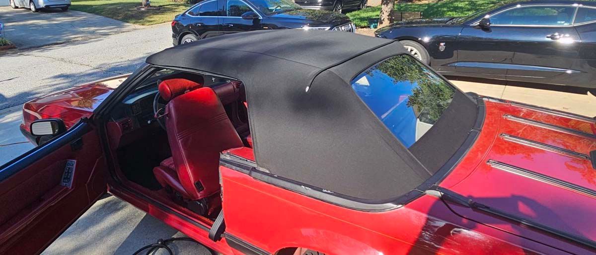 Red convertible with a black top. The car door is open, with a red interior. Other cars are in the background.
