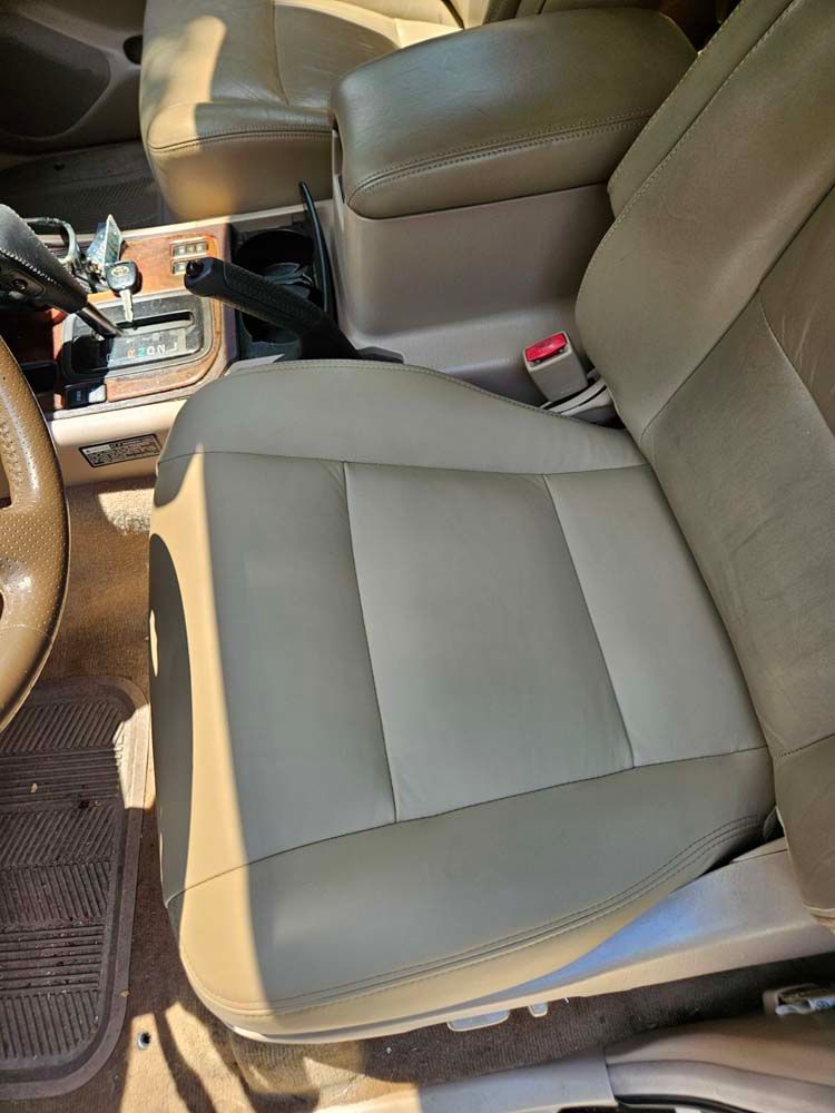 Beige leather car seat with center console and steering wheel visible.