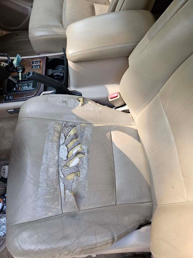 Beige leather car seat, torn and worn, with visible damage.