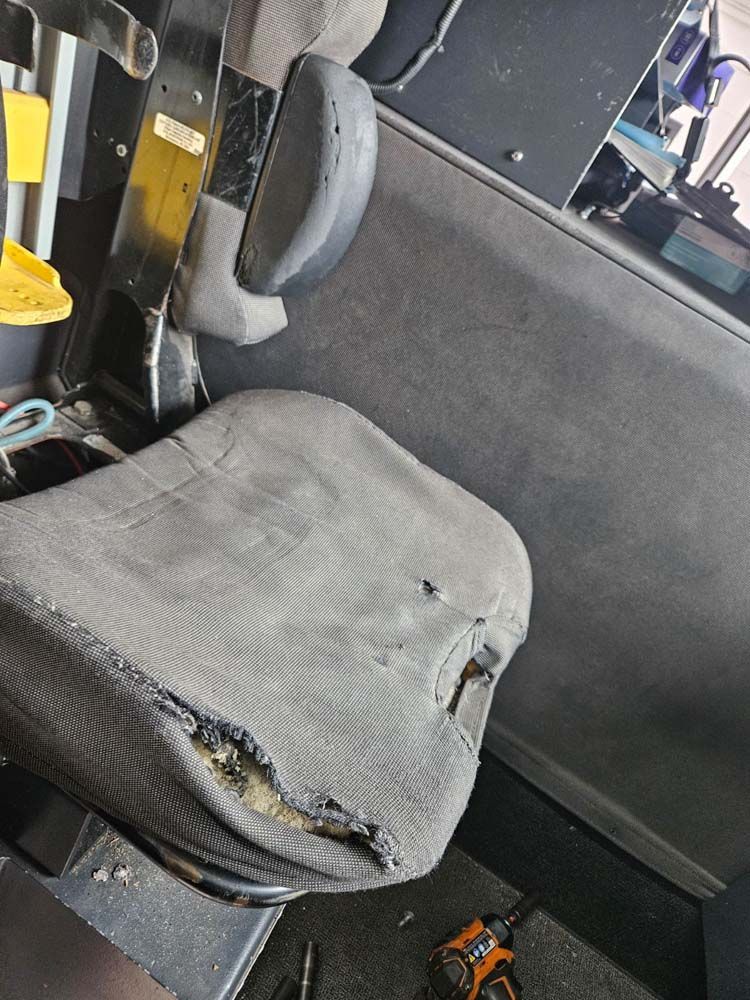 Damaged black seat with worn fabric. Appears to be in a vehicle, with tools visible.