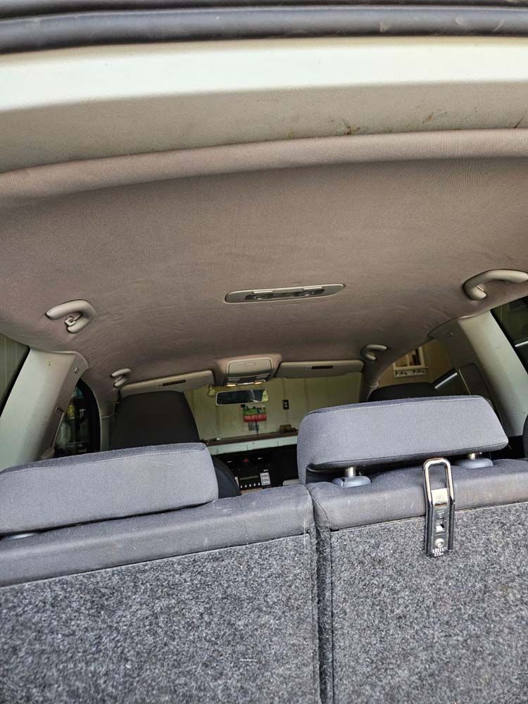 Interior of a car; gray rear seats with headrests, light-colored roof, grab handles, and a center light fixture.