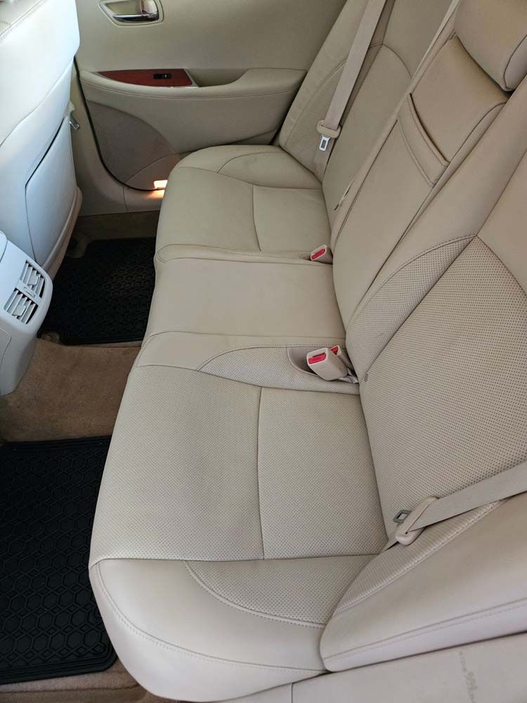 Beige leather car backseat with two black floor mats.