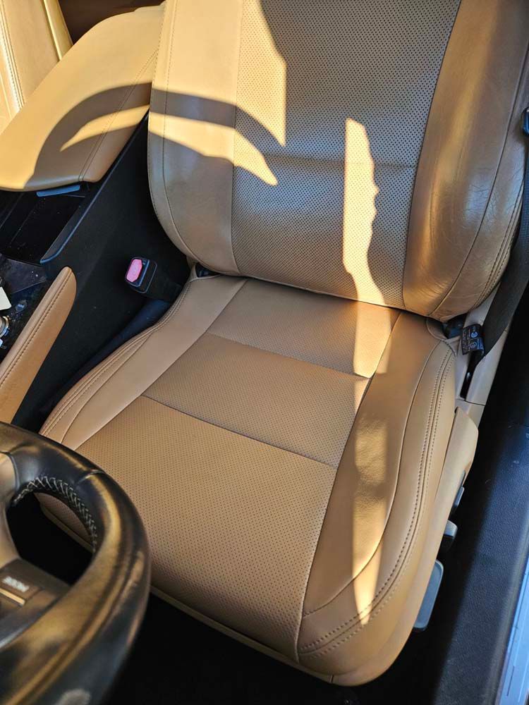 Tan leather car seat with a black steering wheel and center console visible.