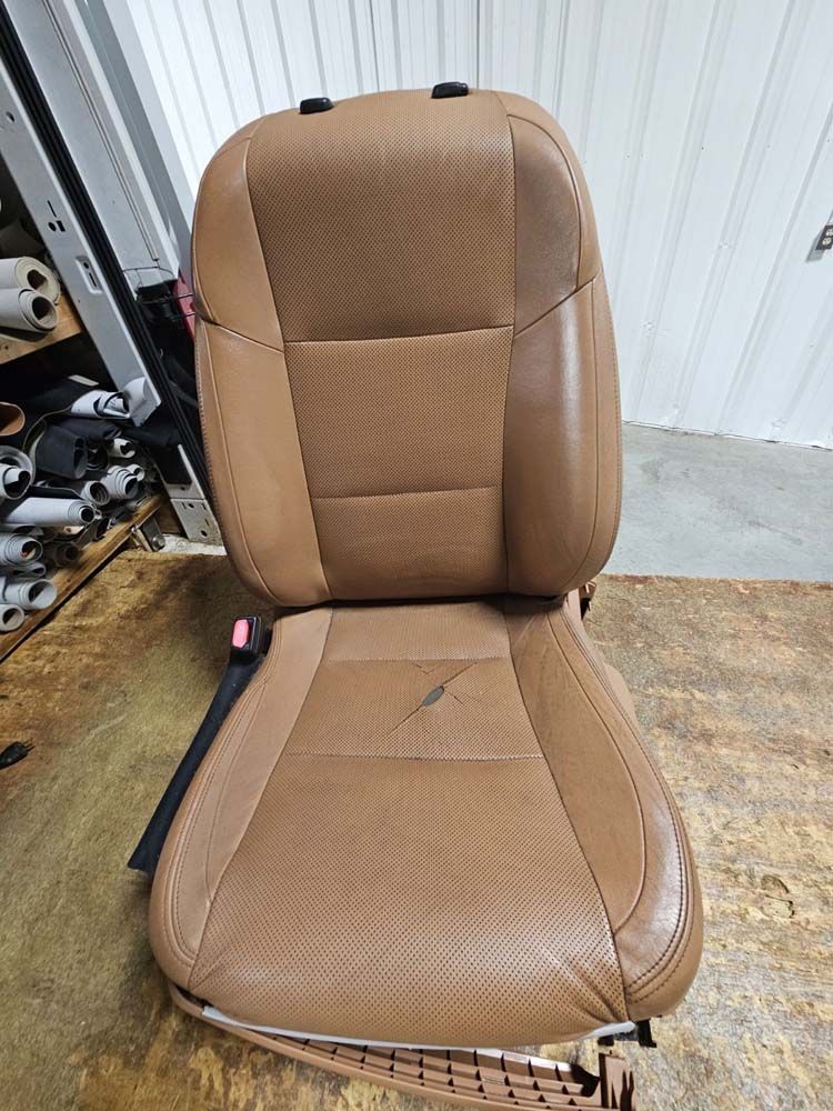 Tan leather car seat with a torn bottom cushion, set on a wooden surface.