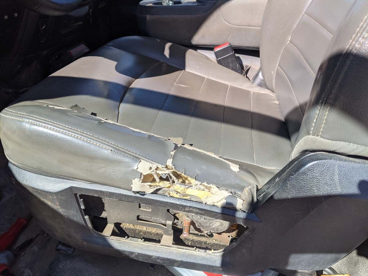 Damaged car seat; tan leather torn revealing foam and metal frame.