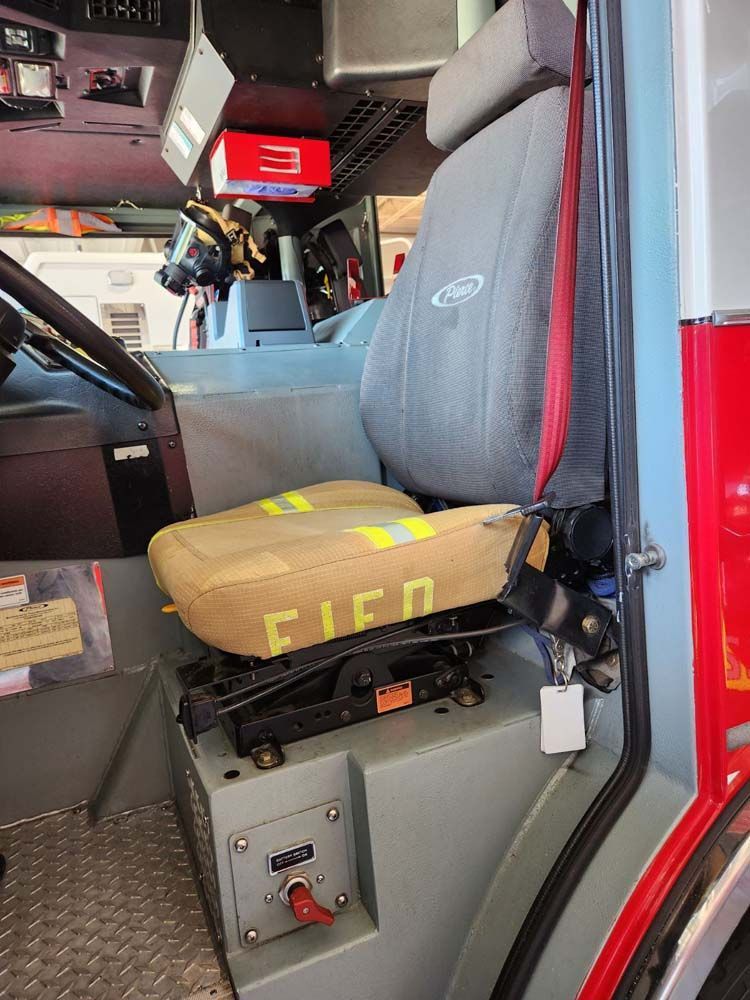 Fire truck interior with gray seat, dashboard, and red and silver trim. Seat has 