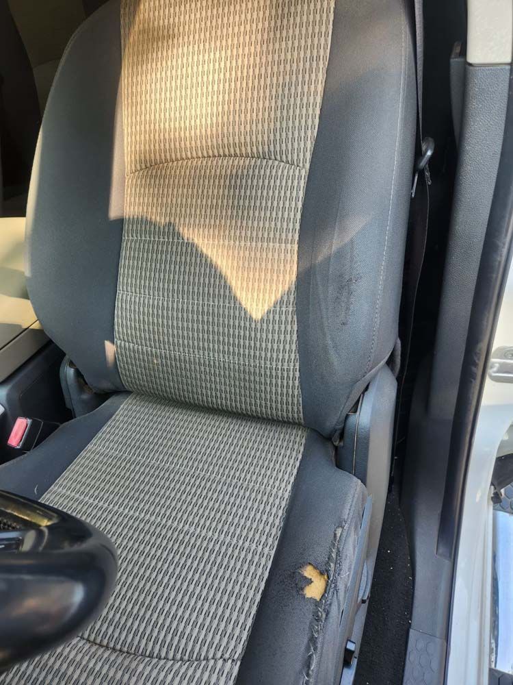 Car seat with gray and tan fabric. A small tear is visible on the seat's side.