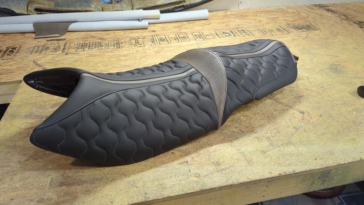Black and gray motorcycle seat with quilted pattern, resting on a wooden surface.