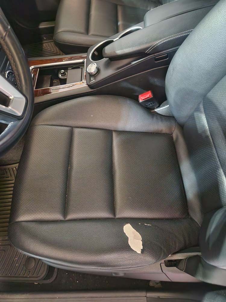 Black leather car seat with torn section. Interior view with steering wheel and center console.