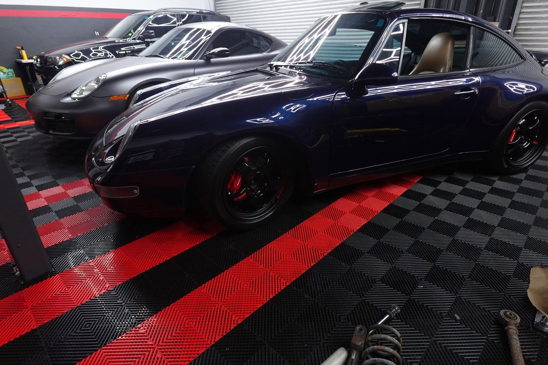 Row of sleek sports cars in a showroom, including a dark blue car with red stripes in the foreground
