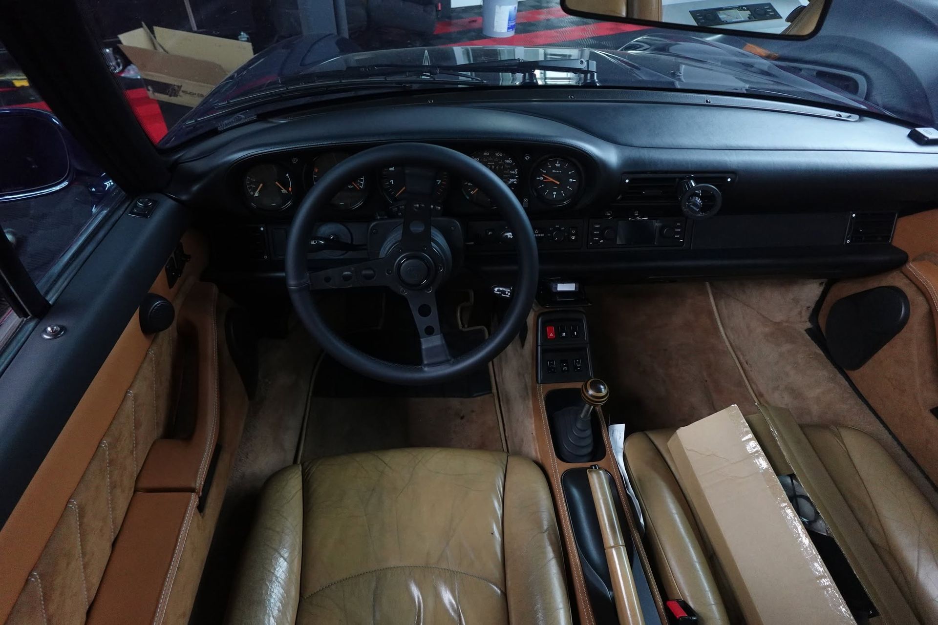 Vintage car interior with tan leather seats, black dashboard, and wooden center console, viewed from the driver’s seat