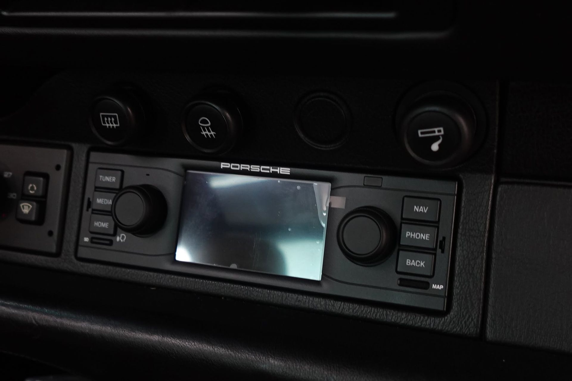 Car dashboard with an in-dash stereo display and control knobs/buttons on a black panel