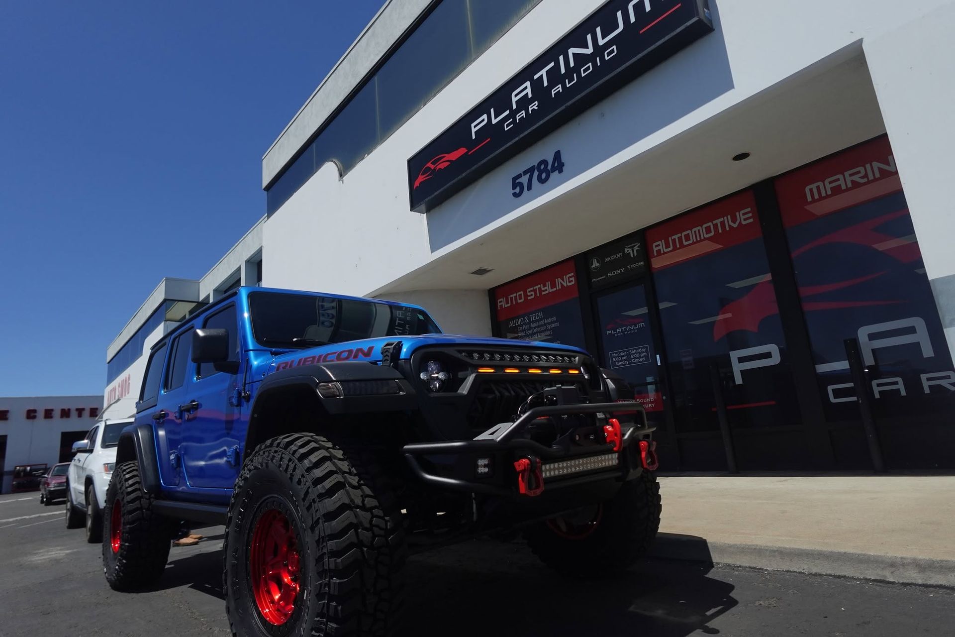 Blue lifted truck parked outside a storefront with red window graphics and the number 5764 above the door