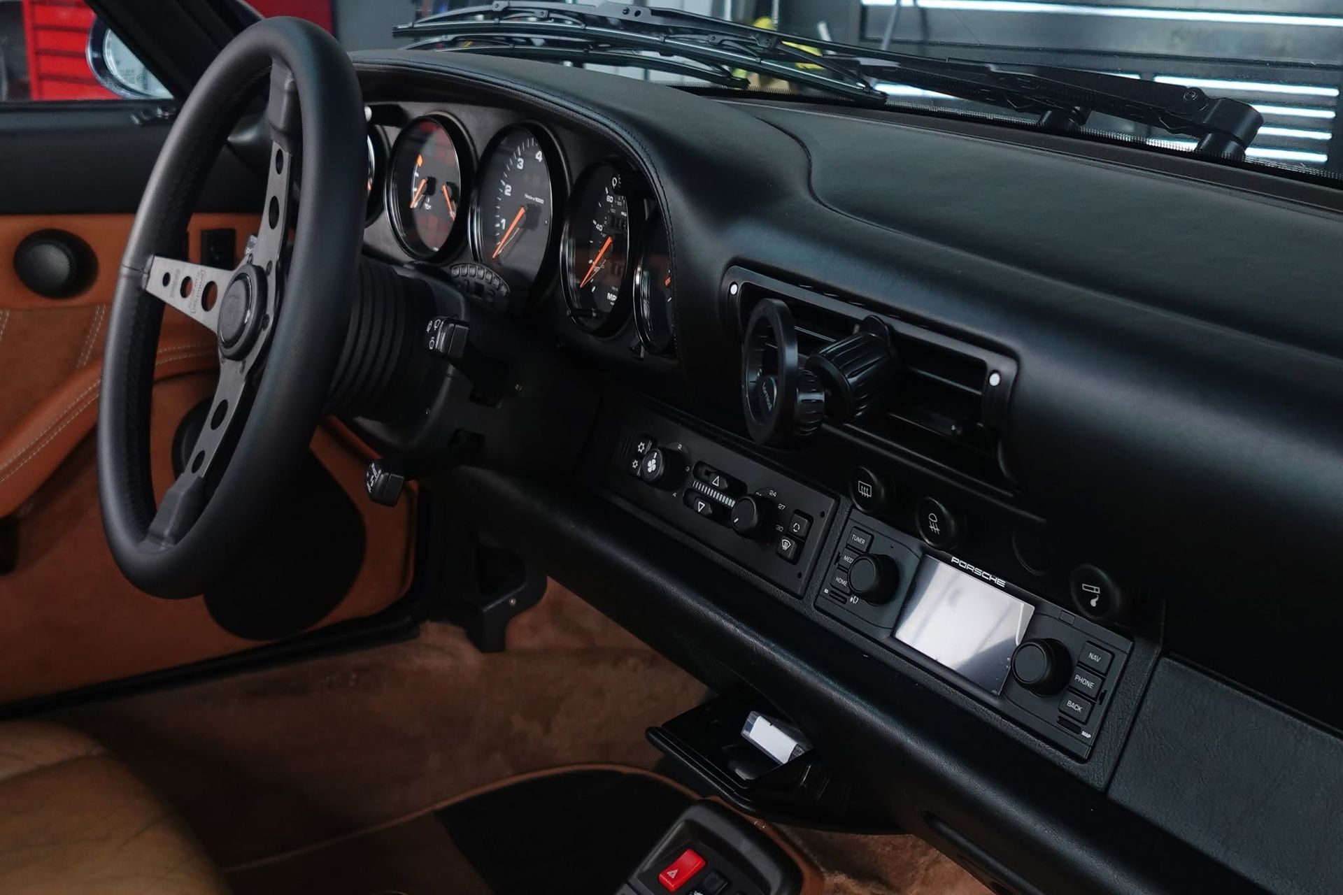 Black car interior with steering wheel, dashboard gauges, and center console, viewed from the driver’s seat