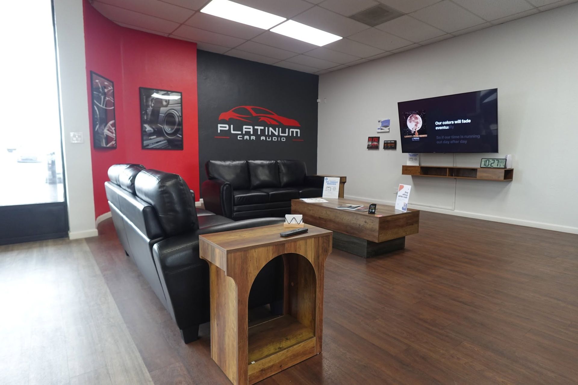 Modern lobby with black leather couches, red accent wall, wooden tables, and wall-mounted TV