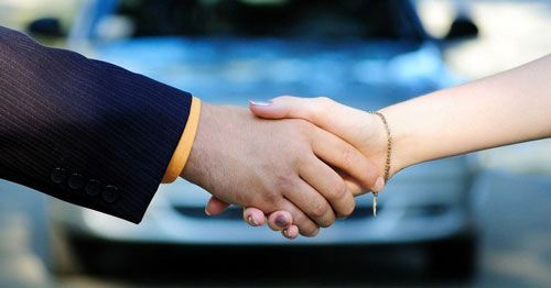 A man and woman shaking hands in front of a car