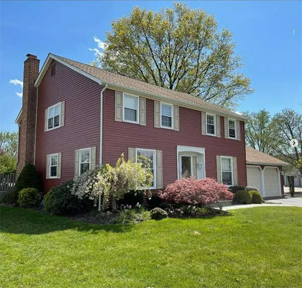Two-story red house with a green lawn, trees, and a brick chimney under a blue sky.