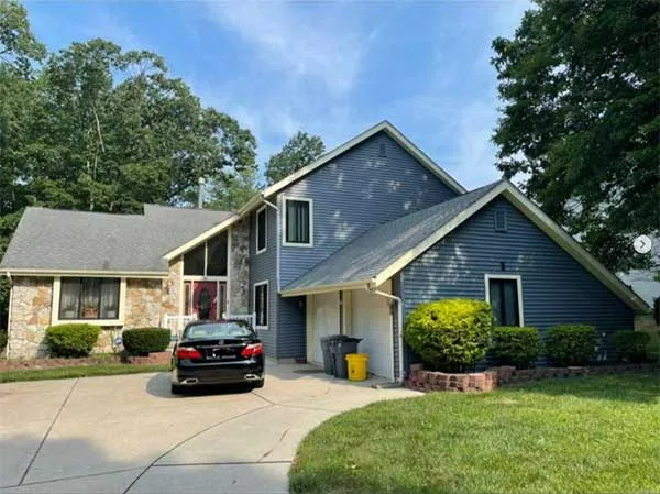 House with blue siding, stone facade, and gray roof, with a black car in the driveway.