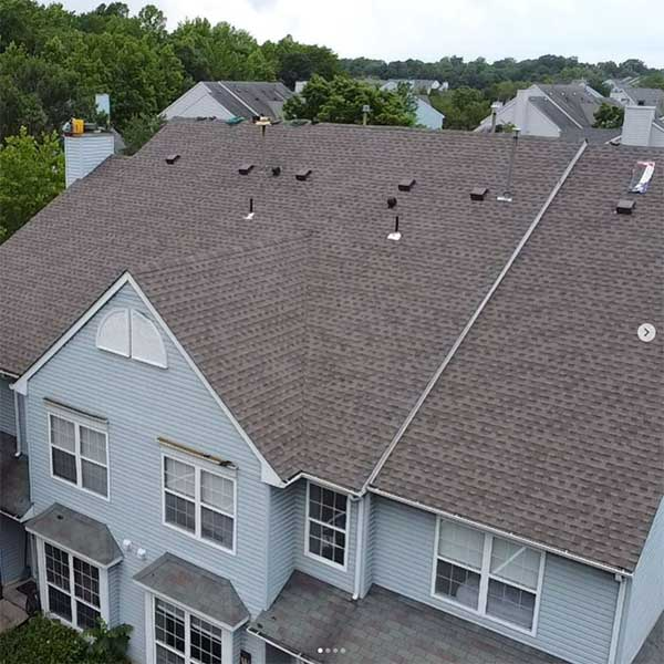 Gray shingled roof on a light blue multi-story house. Trees are in the background.