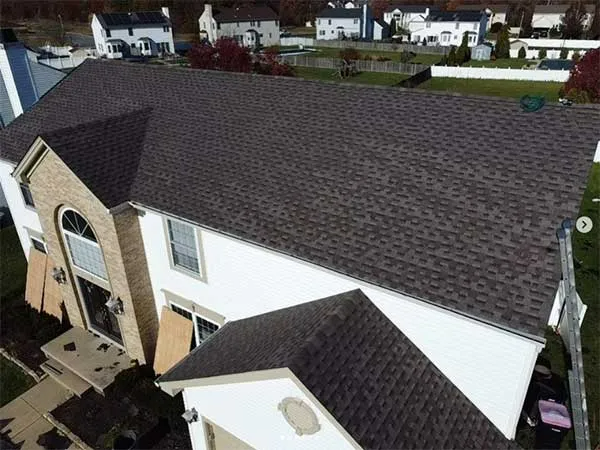 Brown shingle roof on a two-story house with a brick facade section; suburban setting with houses in the background.