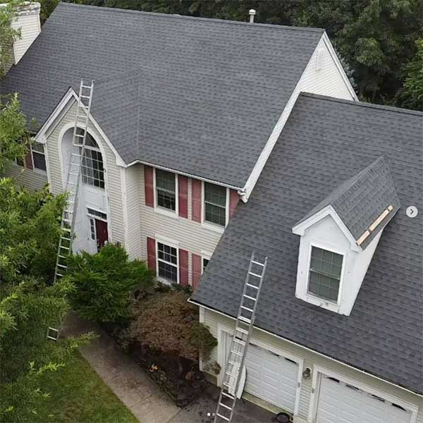 House with gray shingle roof, ladders, and white siding, viewed from above. Garage and front door visible.