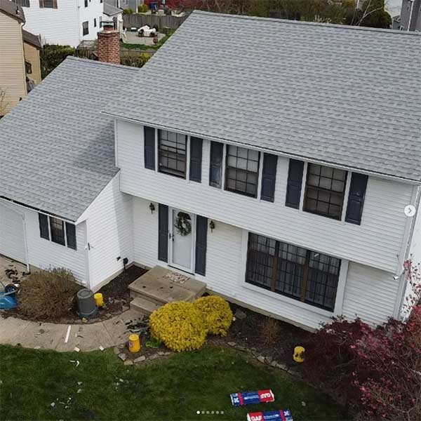 White two-story house with gray roof, black shutters, and front door with a wreath.
