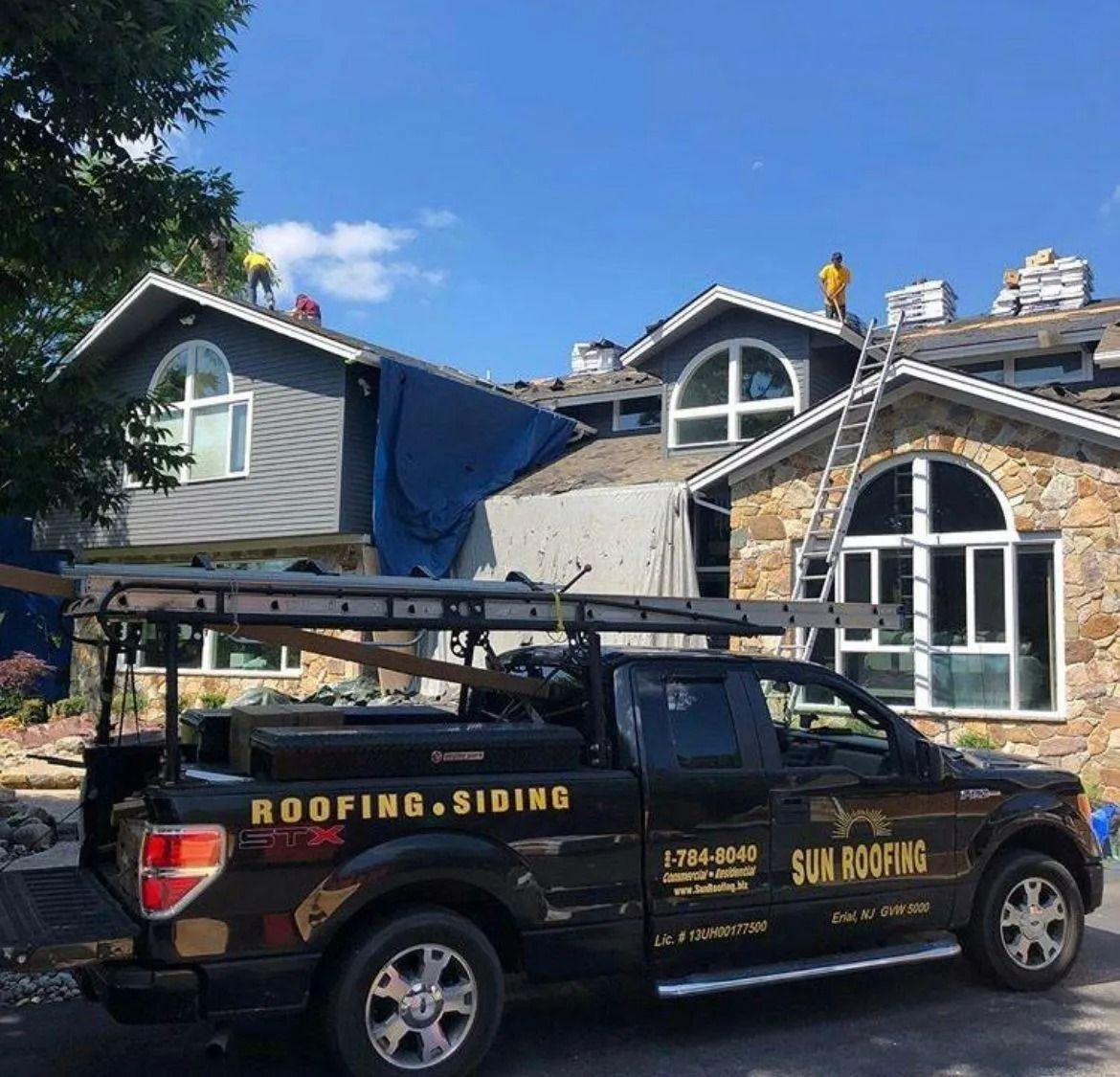Black truck parked in front of a house. Roofers on the roof. Sky is blue.