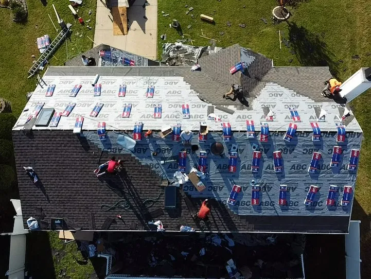 Roofers working on a residential roof, laying shingles and underlayment.