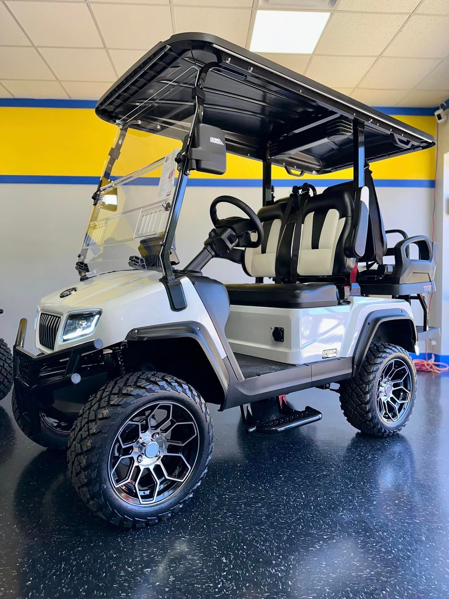White lifted golf cart with black roof, tires, and seating, parked indoors with a blue and yellow wall.