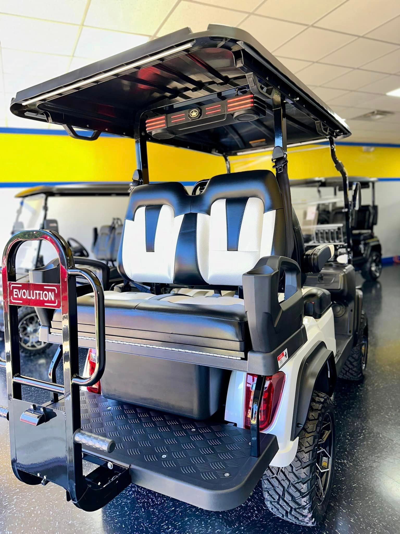 A white golf cart with black and white seats, black roof, and off-road tires is parked in a showroom.