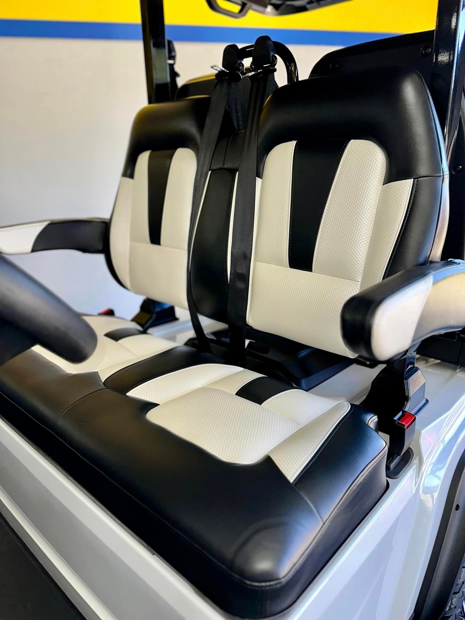 Golf cart seats with black and white leather. The seat has a two-toned pattern and a black seatbelt.