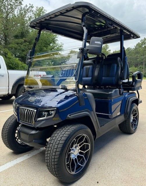 A blue golf cart is parked in a parking lot next to a truck.