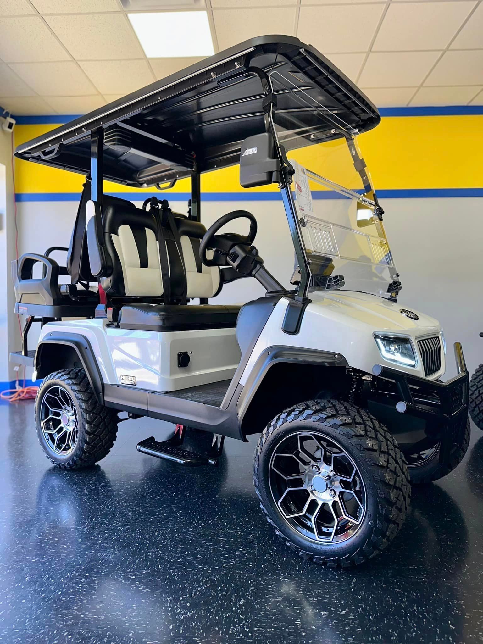 White golf cart with black accents and oversized wheels, parked indoors against a wall with yellow and blue trim.