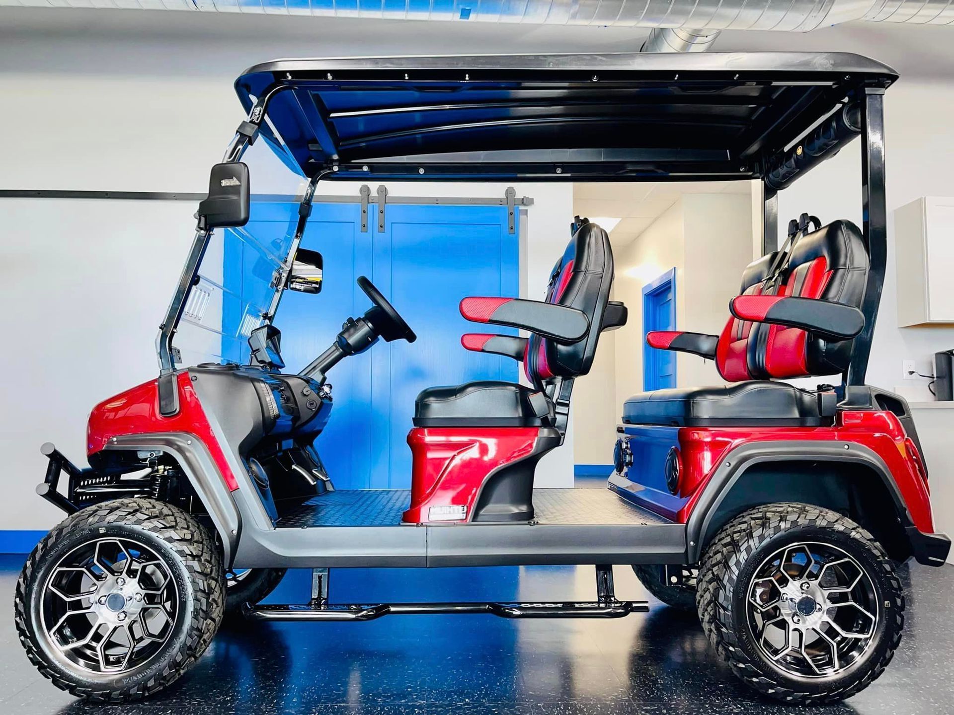 A red golf cart is parked in a garage next to a blue door.