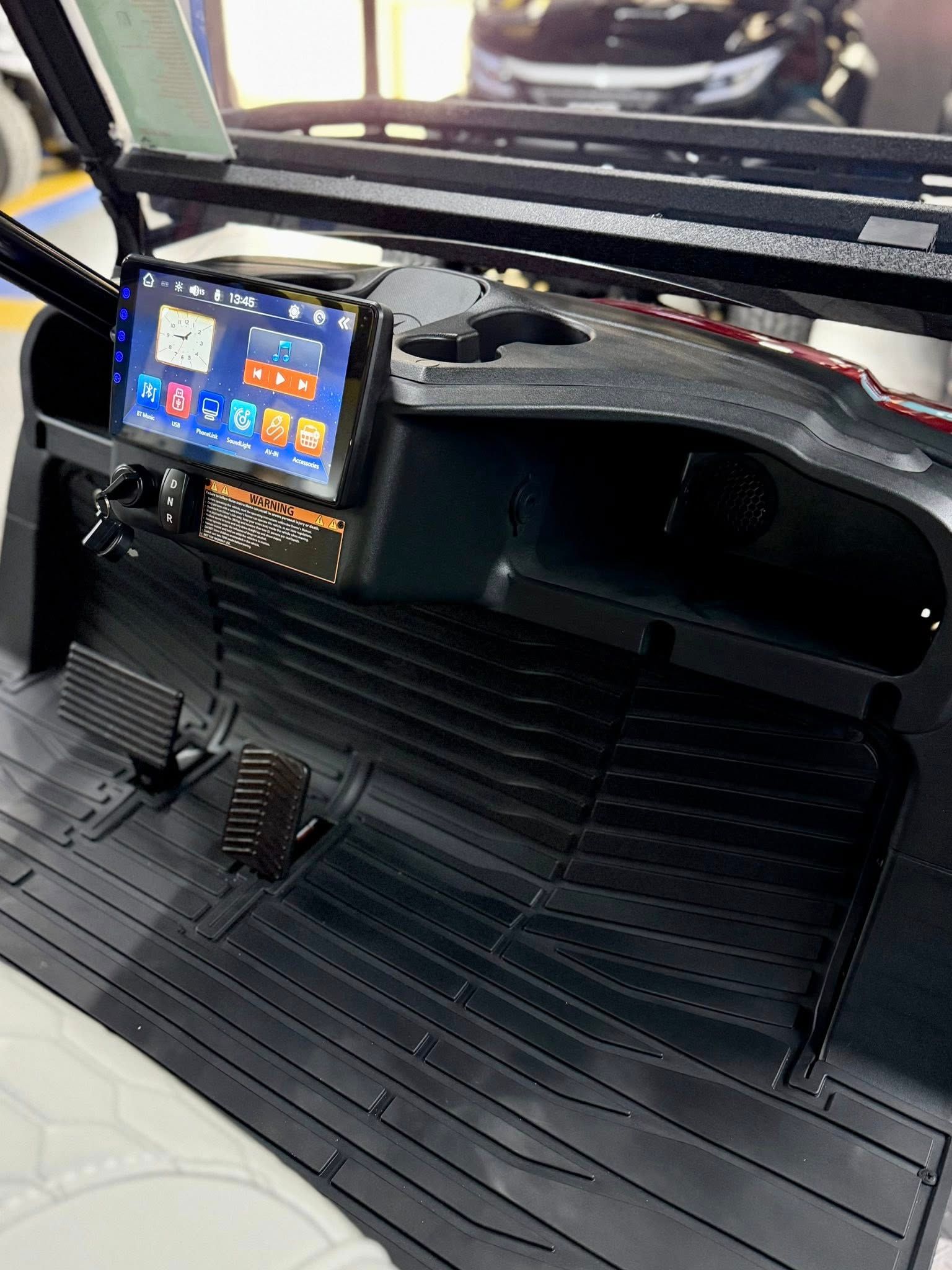 Black golf cart interior with touchscreen, pedals, and rubber floor mat.
