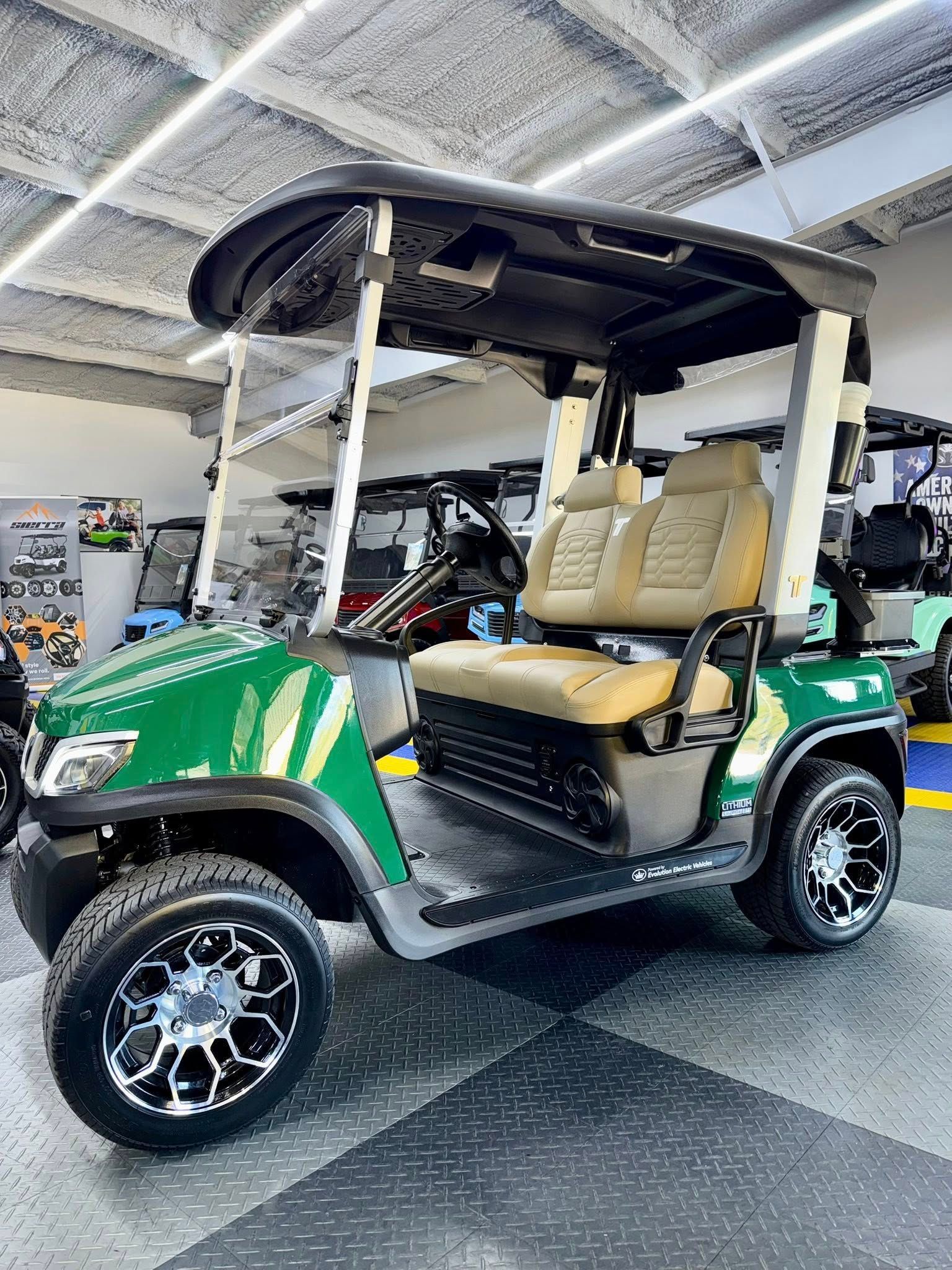 Green golf cart with black roof and wheels, tan seats, inside a shop.