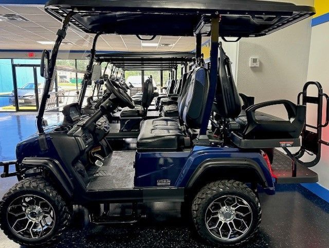 Navy blue golf cart with black seats and silver wheels, parked indoors. Additional golf carts are visible in the background.