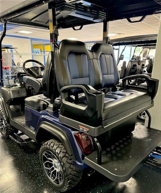 Navy blue golf cart with black and blue seats, black roof, and large tires, parked indoors.