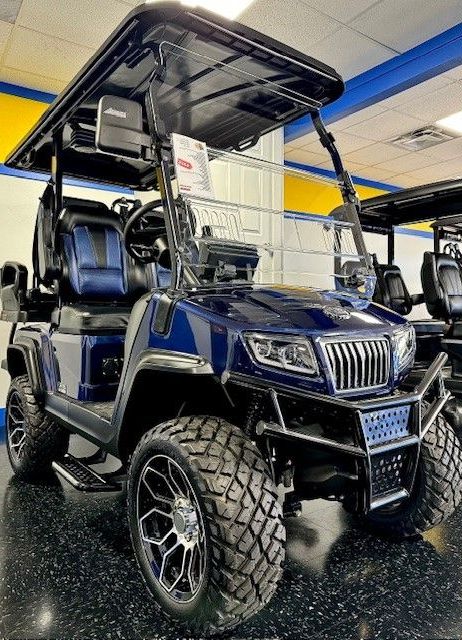 Dark blue golf cart with off-road tires, black roof, and chrome accents displayed indoors.
