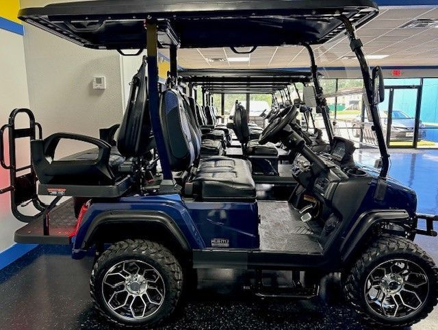 Row of blue golf carts parked indoors. Each cart has black seats, wheels, and a canopy.