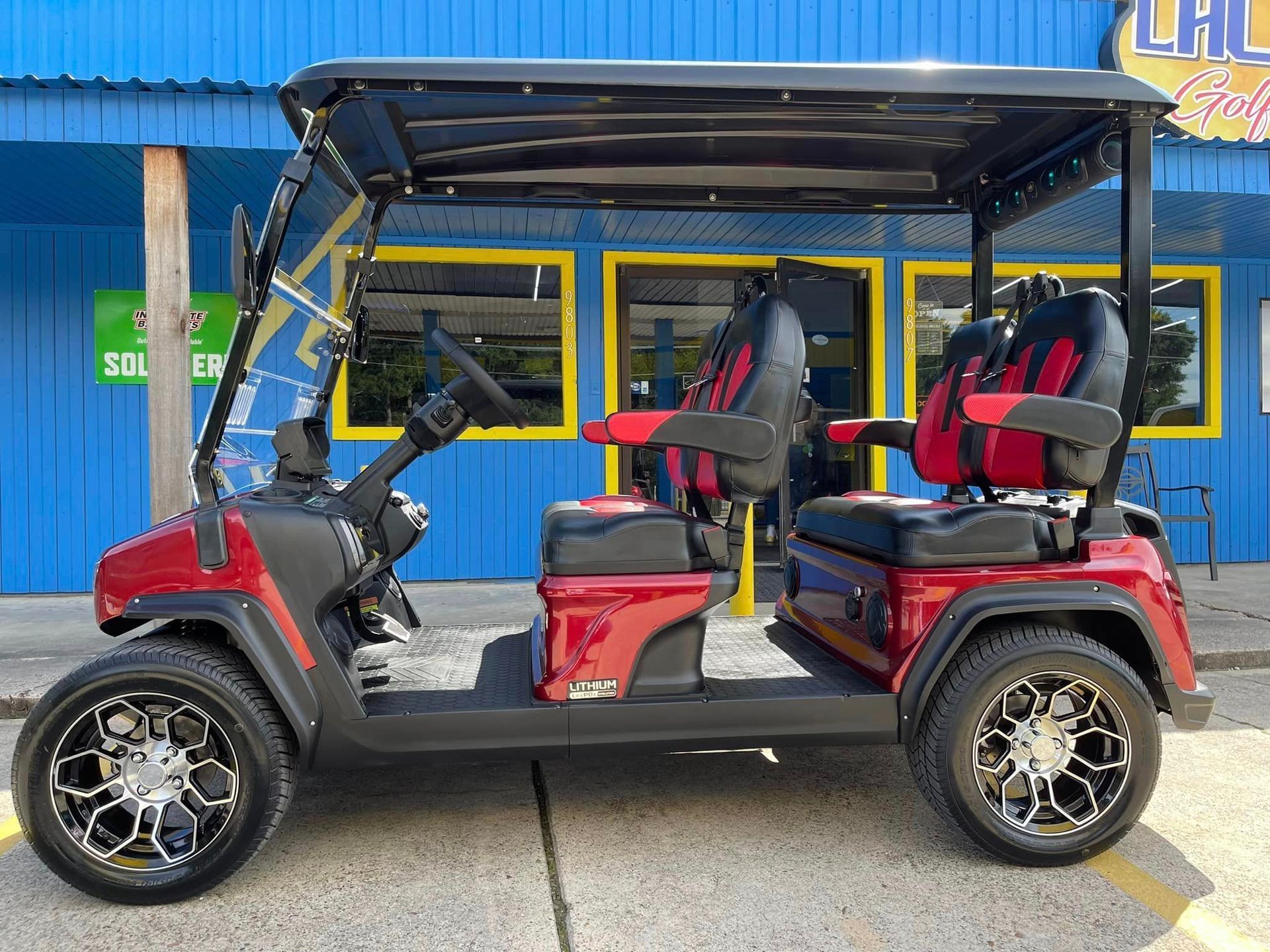 A red golf cart is parked in front of a blue building.