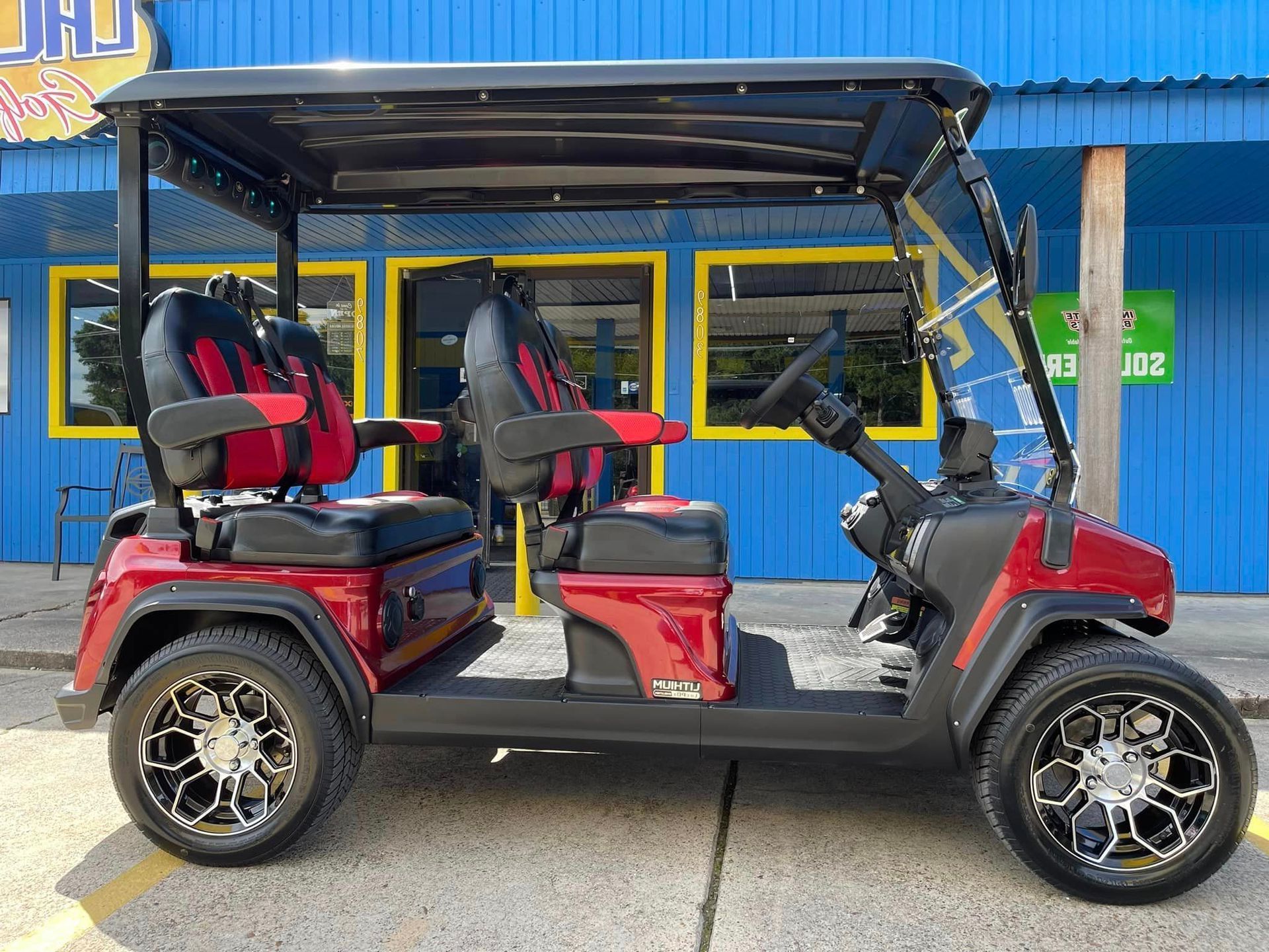 A red golf cart is parked in front of a blue building.