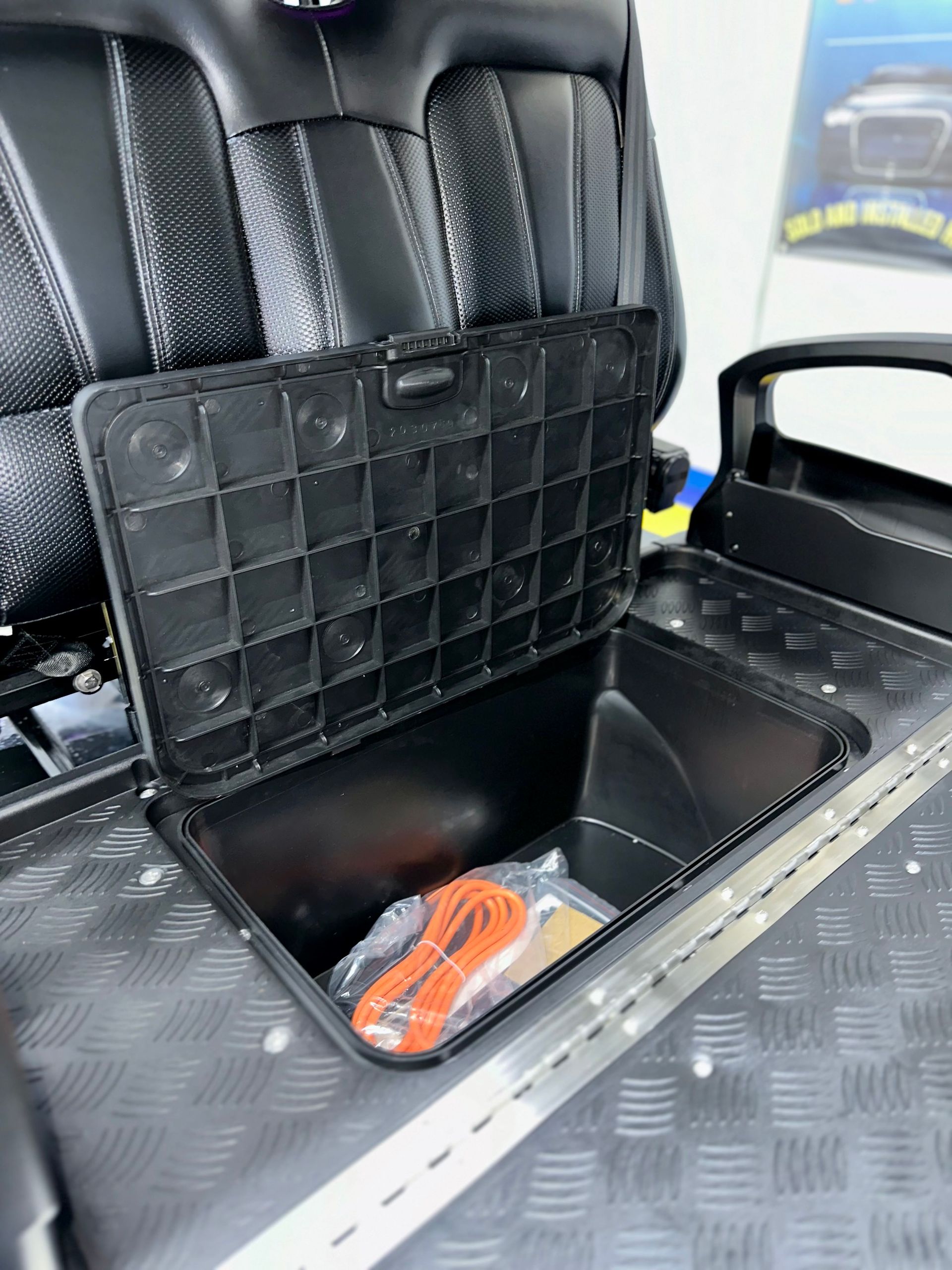 The back seat of a golf cart has a storage box underneath it.