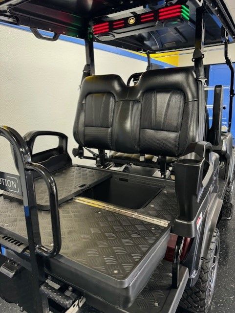 Black golf cart with diamond plate bed, black seats, and a rear-facing seat. Red and green lights on top.