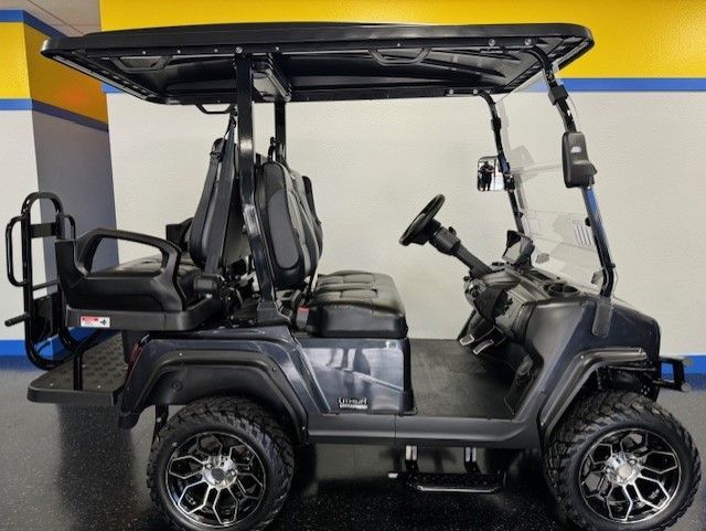 A dark gray golf cart with black seats and a canopy, sporting black wheels and a windshield, is parked indoors.