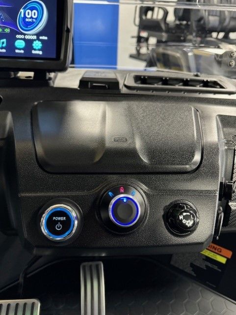 Dashboard of a small electric vehicle with controls, including a power button, climate control dial, and hazard lights button.