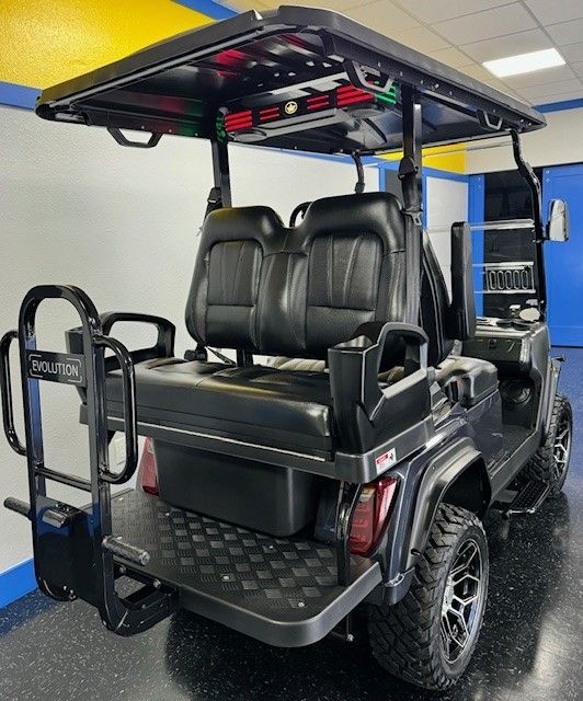 Black golf cart with rear-facing bench seat, black seats, and a black roof. The golf cart is parked indoors.