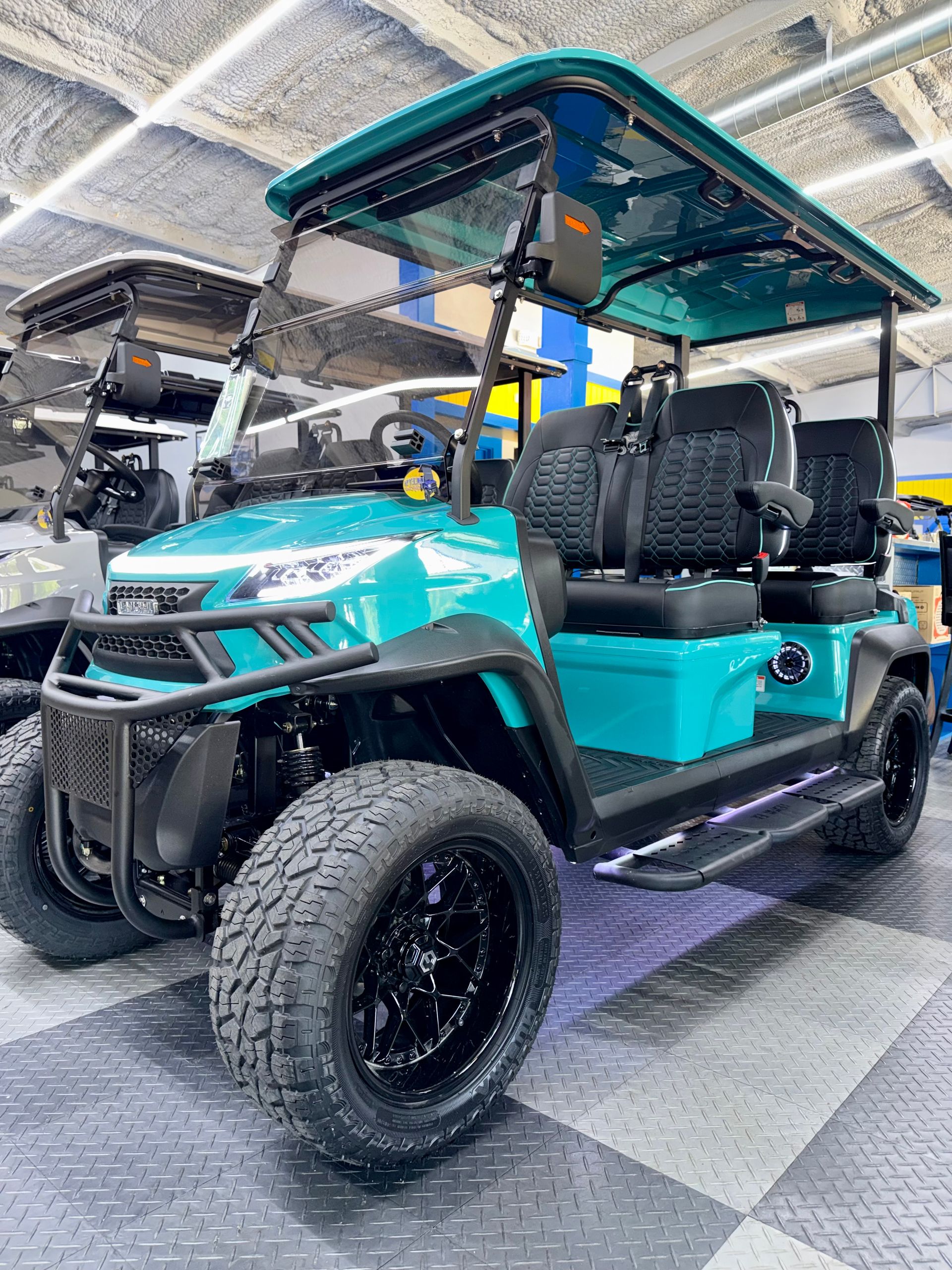 Turquoise golf cart with black tires and roof parked indoors on checkered floor